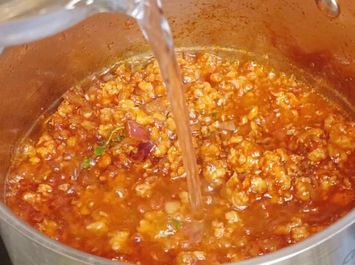 Clear water being poured into a pot containing the savory, rich meat sauce.