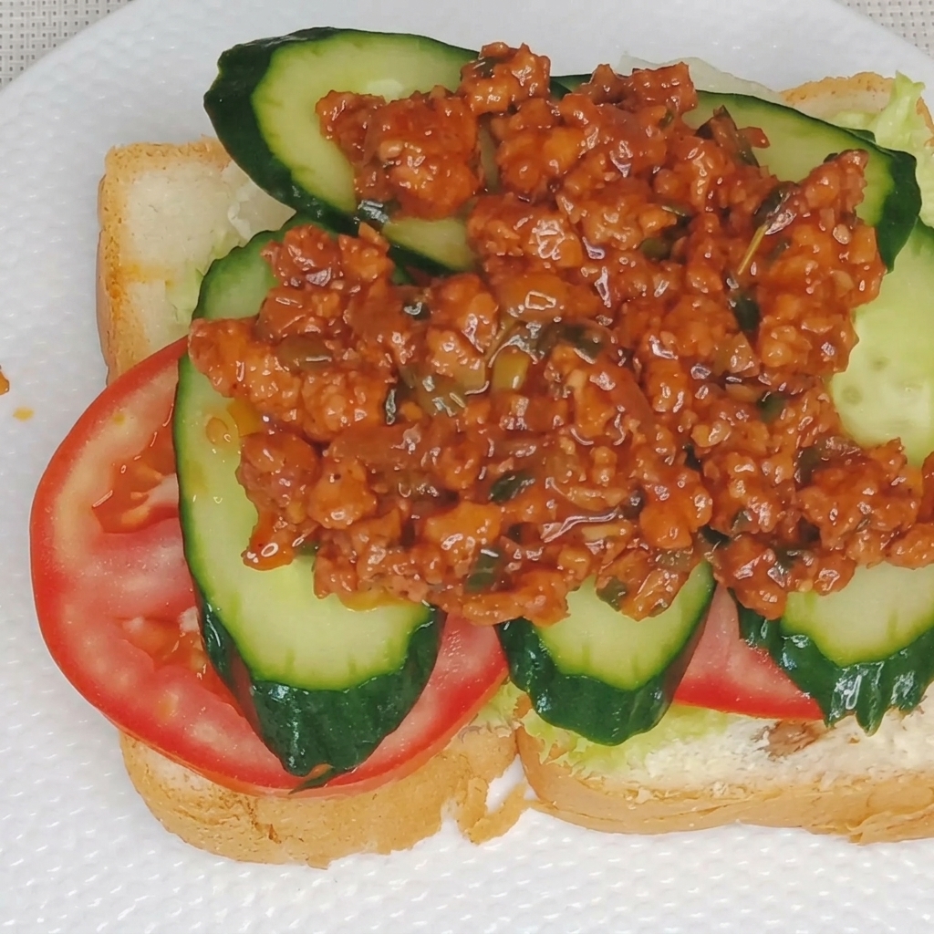 Close-up of creamy egg yolk sauce being drizzled over a layer of meat sauce on a sandwich.