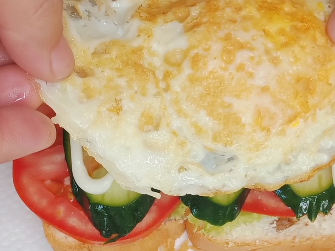 A perfectly fried egg being placed atop the assembled sandwich layers.