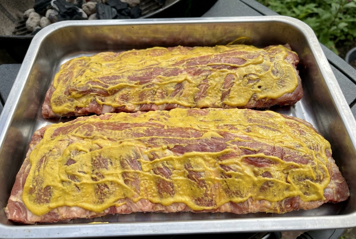 Two racks of ribs coated in yellow sauce sitting on the grill grates, ready to be smoked.