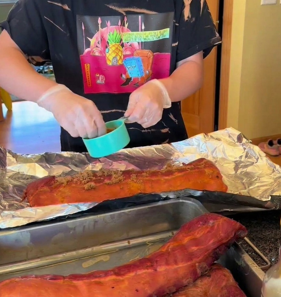 Smoked ribs on aluminum foil being seasoned with a dry rub and drizzled with honey.
