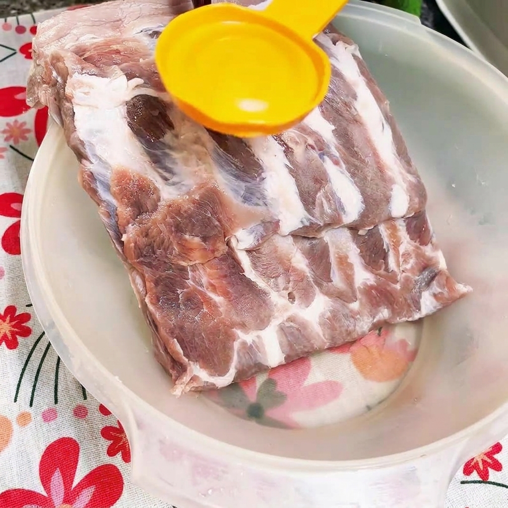 Dark oyster sauce being poured onto raw pork ribs in a white bowl.