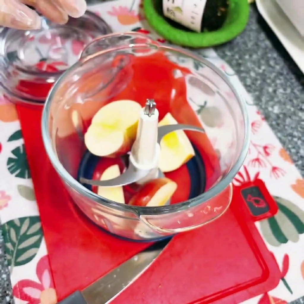 Chopped apple pieces inside a glass electric food chopper.