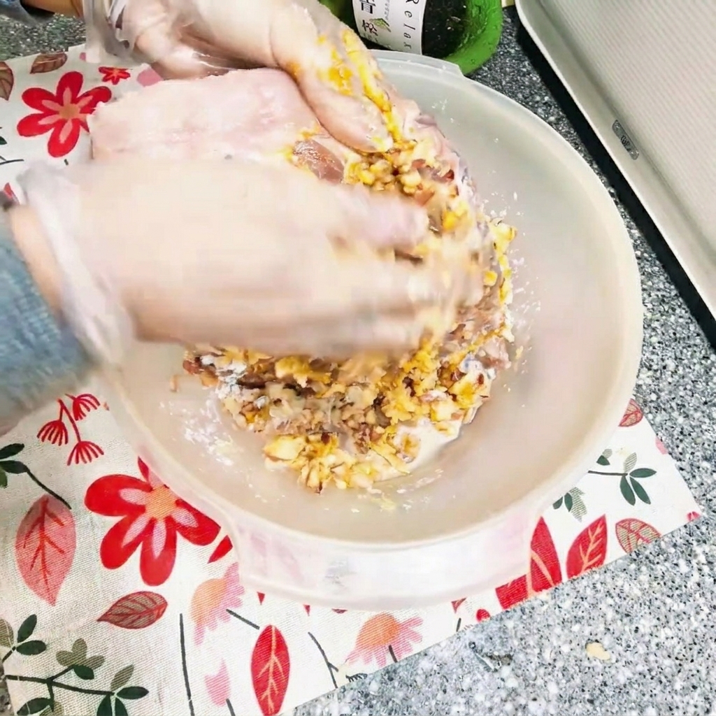 Hands rubbing a thick marinade mixture into raw pork ribs inside a mixing bowl.