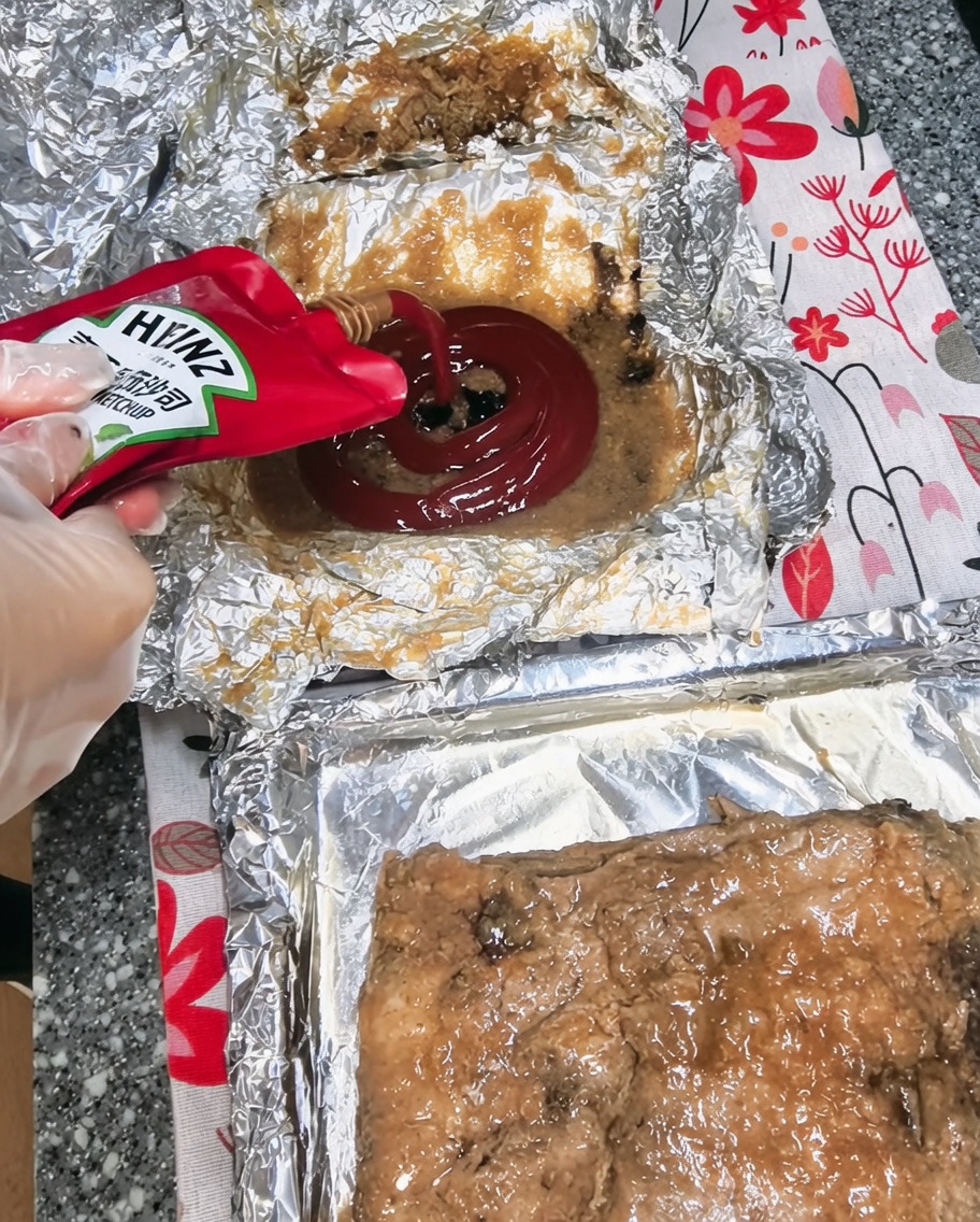 Ketchup being squeezed into a bowl containing cooking juices and other sauce ingredients.