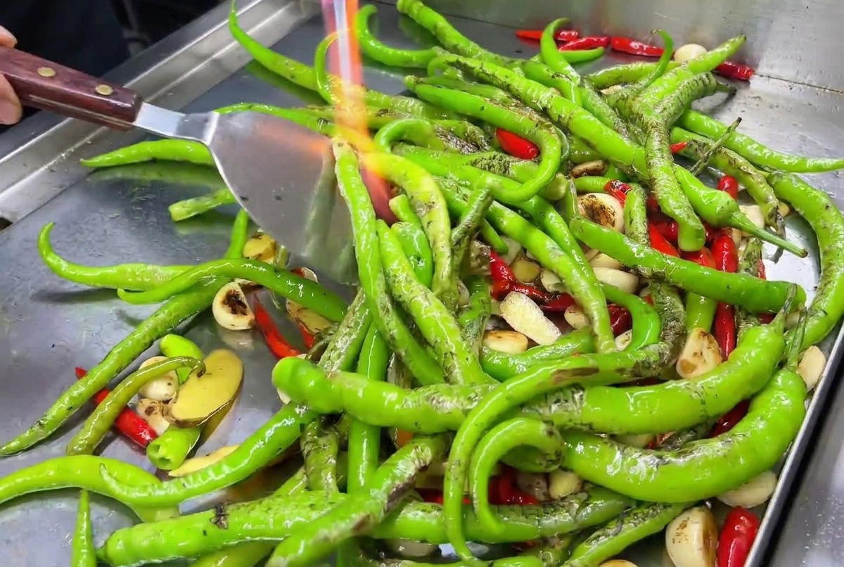 Garlic cloves and red chilies being seared on a hot griddle with a blowtorch flame.