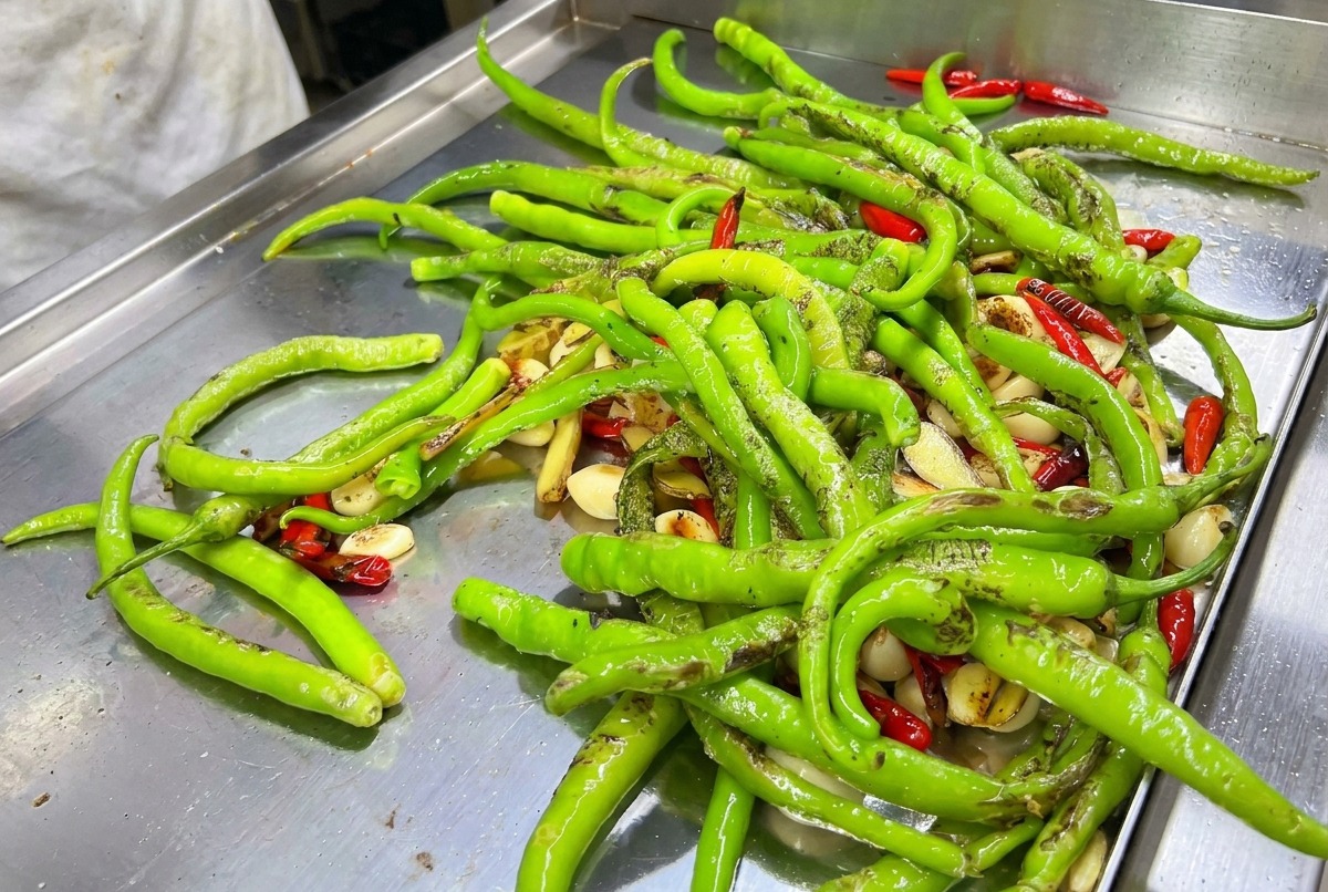 A mix of green and red chilies being blowtorched on a hot griddle.