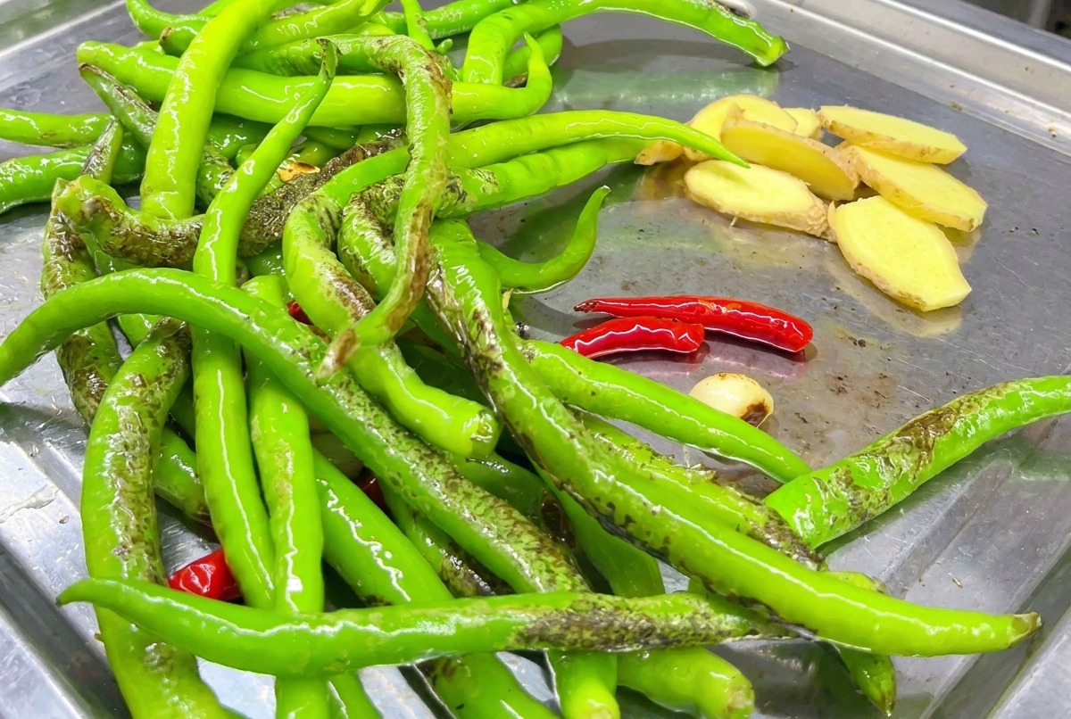 Ginger slices being seared on the griddle with chili peppers.
