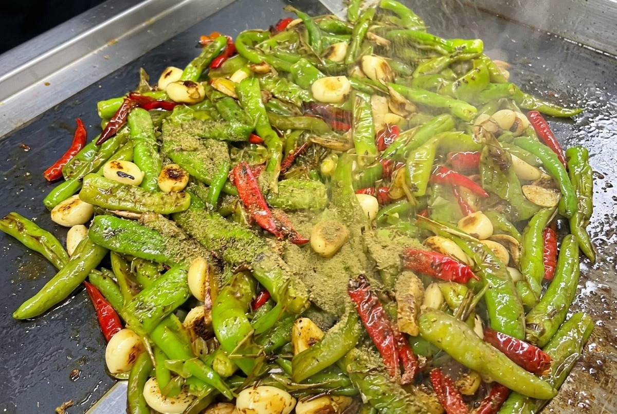 Seasonings and sauces added over charred peppers on a hot griddle.