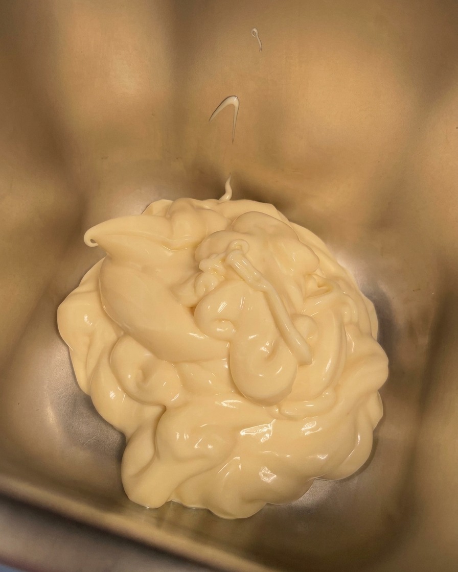 A small bowl of cream being poured into a metal container already holding creamy mayonnaise.