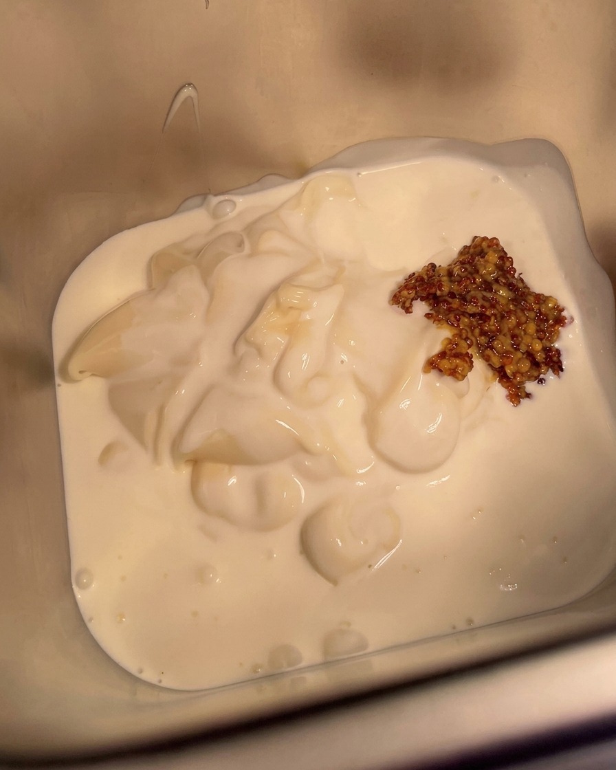 A spoonful of mustard being added to the creamy base in the metal container.