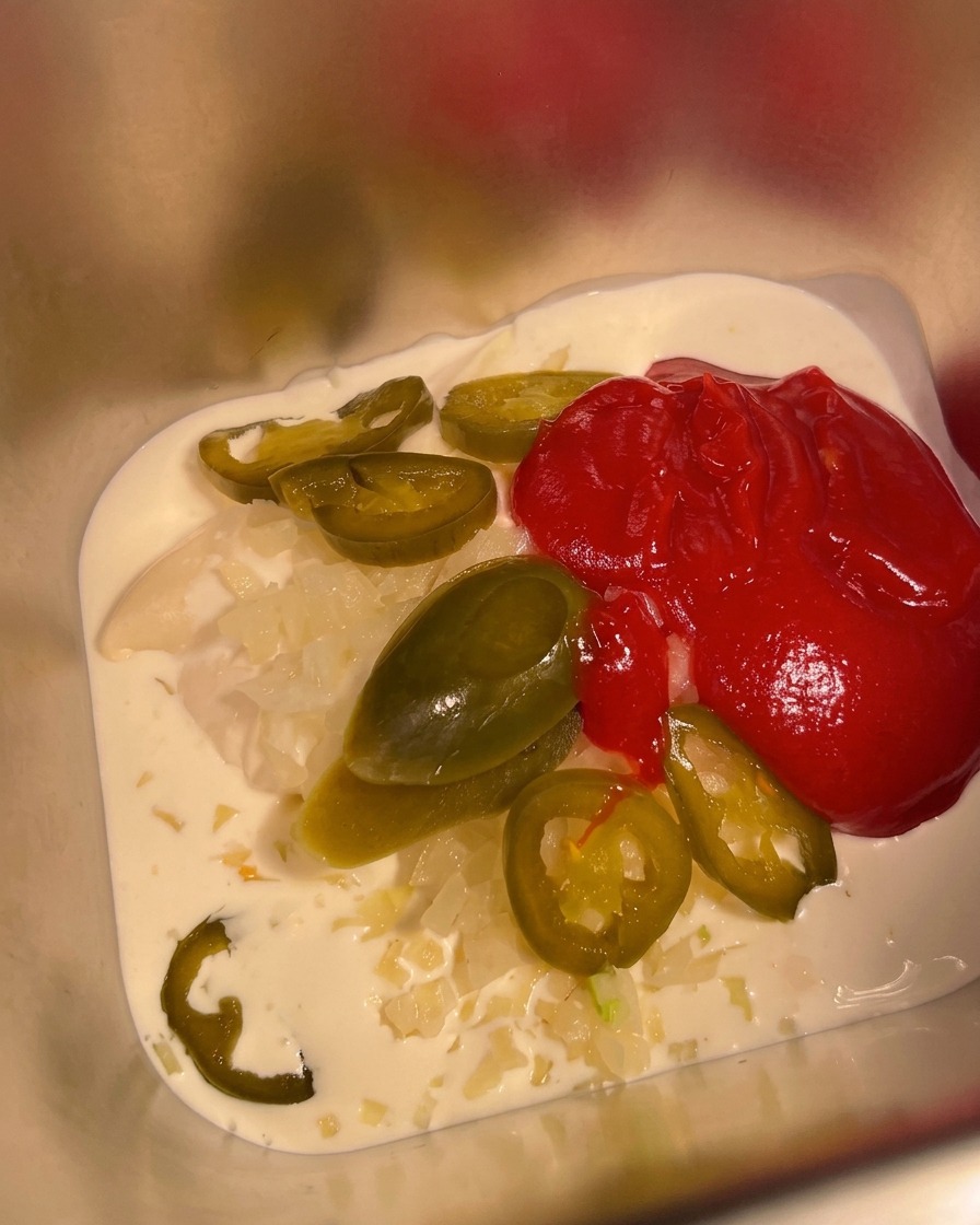 Mexican hot sauce being poured into a metal container already containing the cream and mayonnaise base.