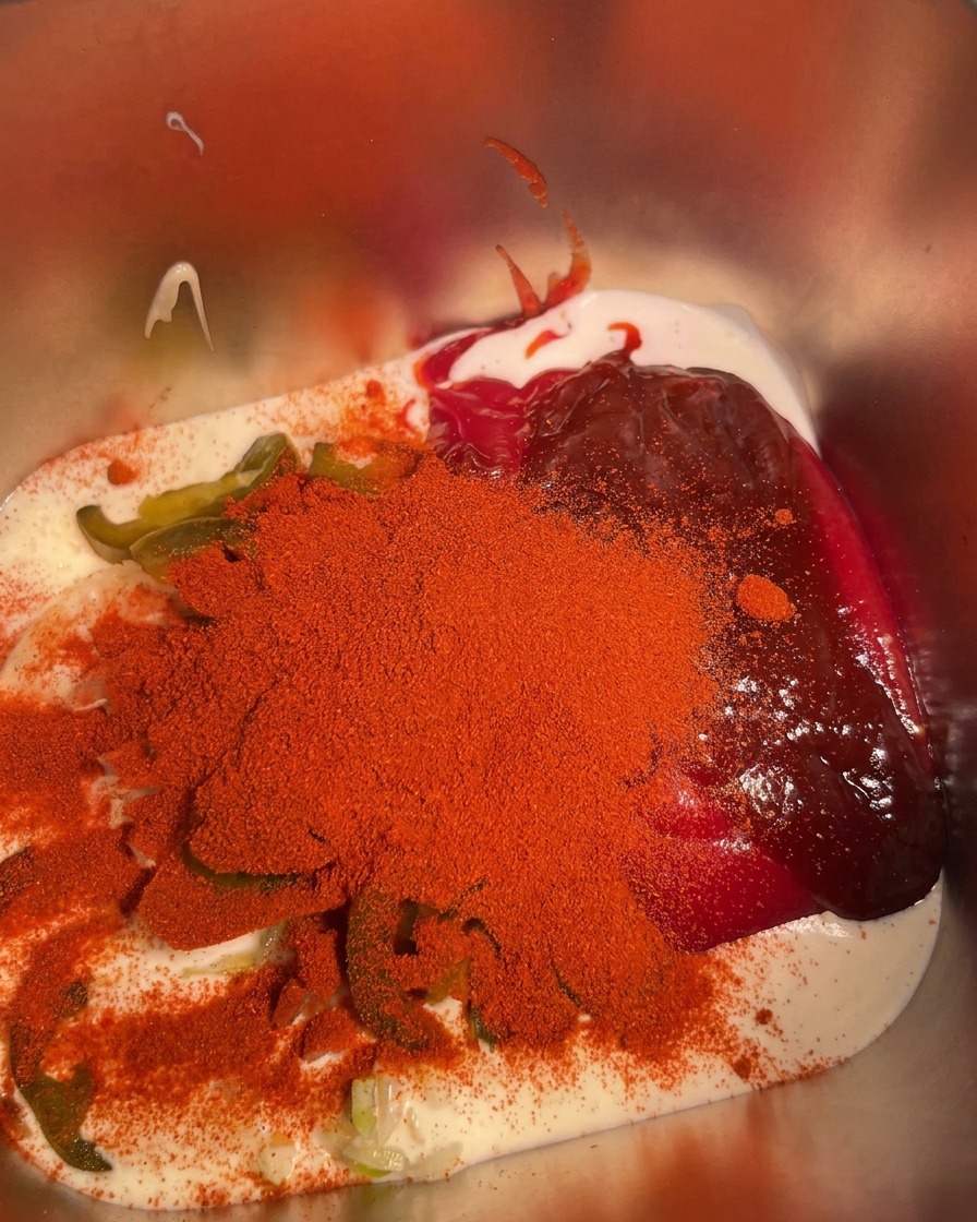 Garlic powder being sprinkled over the combined ingredients in the metal container.