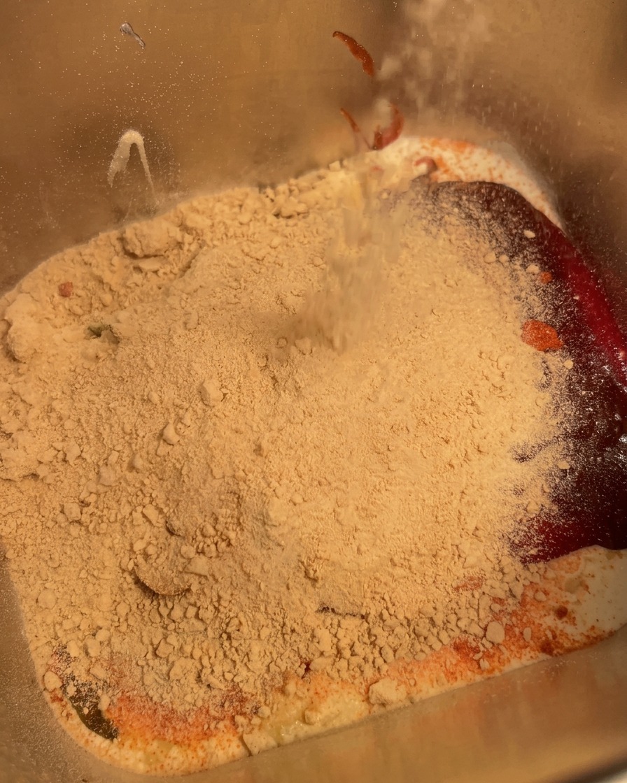 A handheld immersion blender mixing the ingredients inside a metal container until combined.