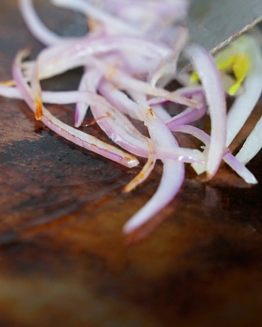 Angus beef brisket strips and red onions being stir-fried together on a hot griddle.