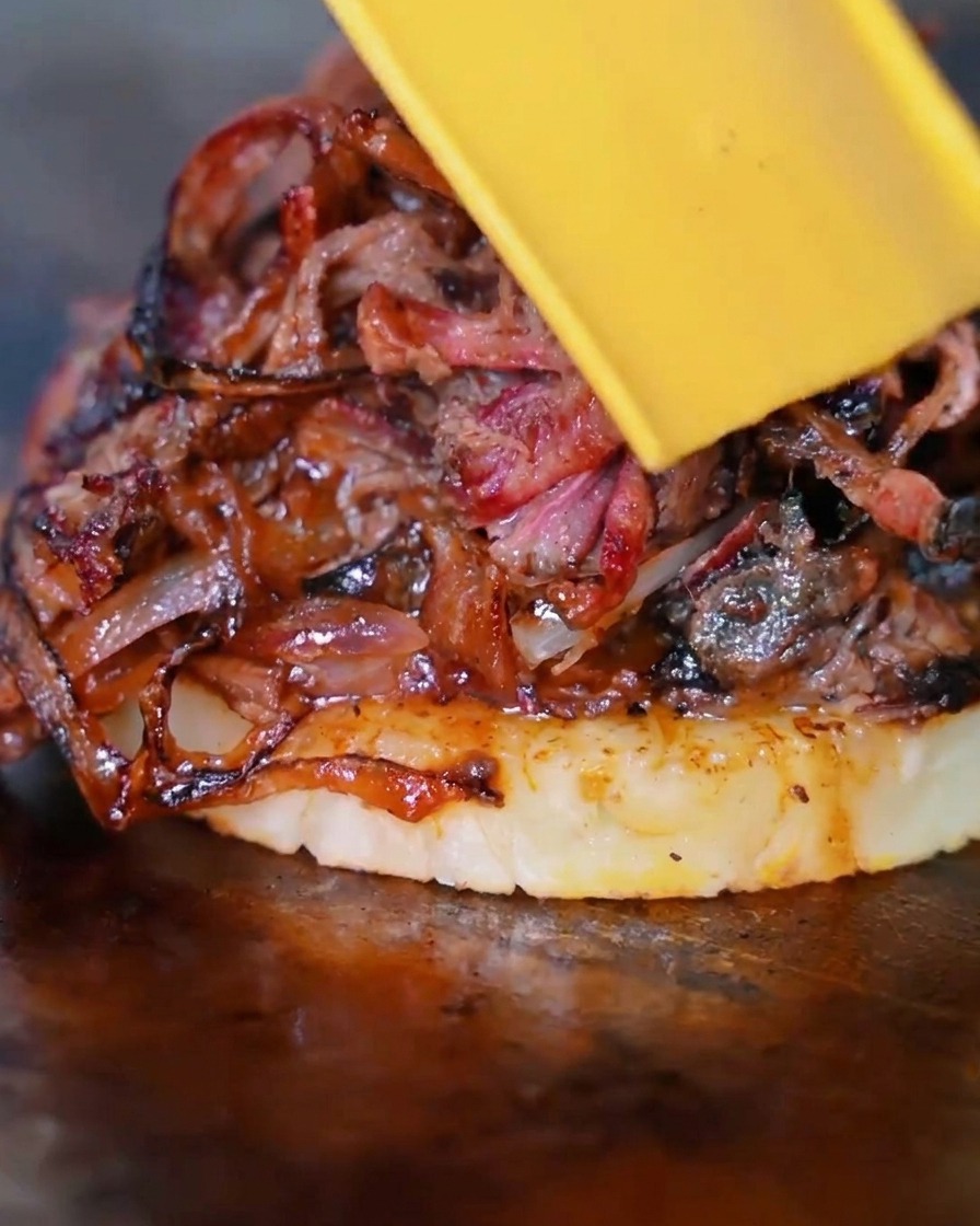 A slice of yellow cheese melting over the beef, onion, and pineapple stack.