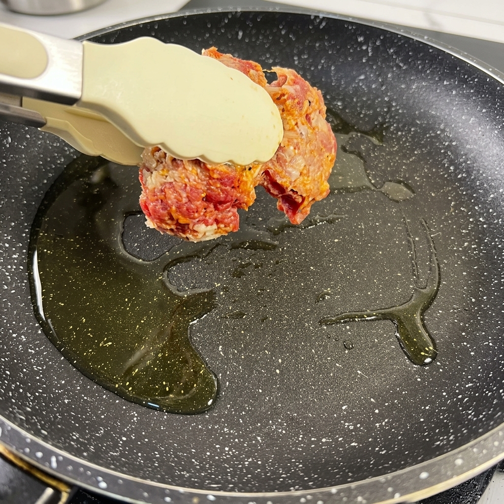 Seasoned beef brisket pieces sizzling in a hot pan with oil, turning a deep brown color.