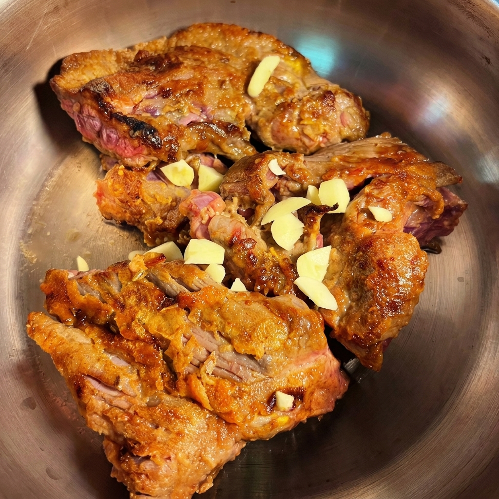 Seared beef brisket pieces being added to a pressure cooker with chopped garlic and onions ready to be cooked.