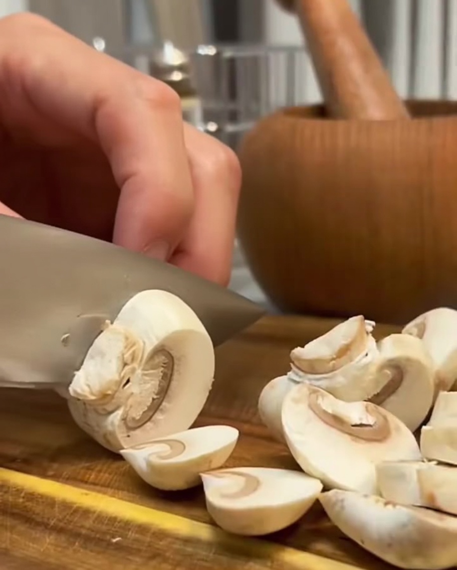 Fresh mushrooms being sliced with a knife on a wooden surface.