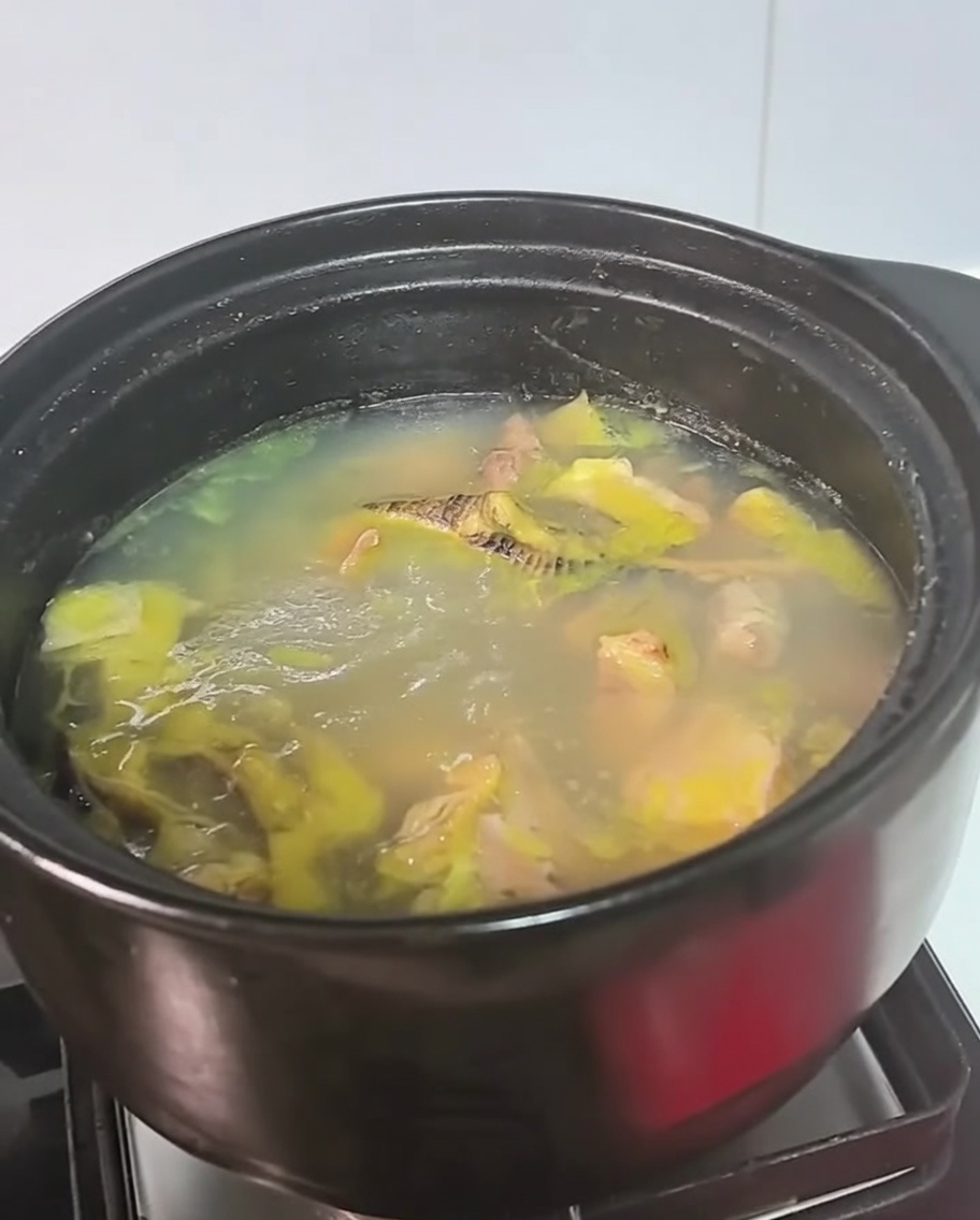 A black pot of chicken soup simmering on a stove burner.
