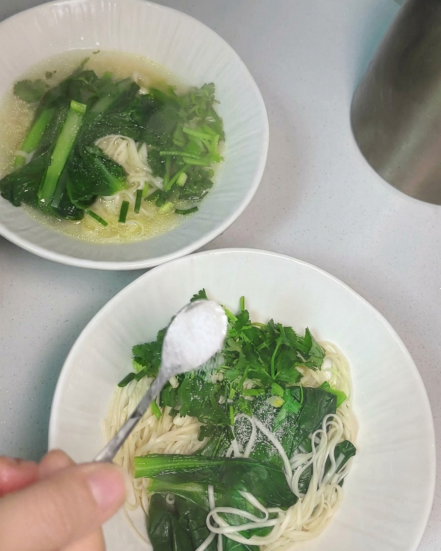 Hot chicken soup being poured from a ladle into a bowl of noodles.
