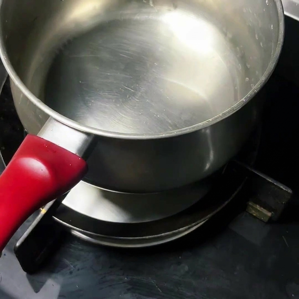 A raw egg frying in a clean stainless steel pot on the stovetop.
