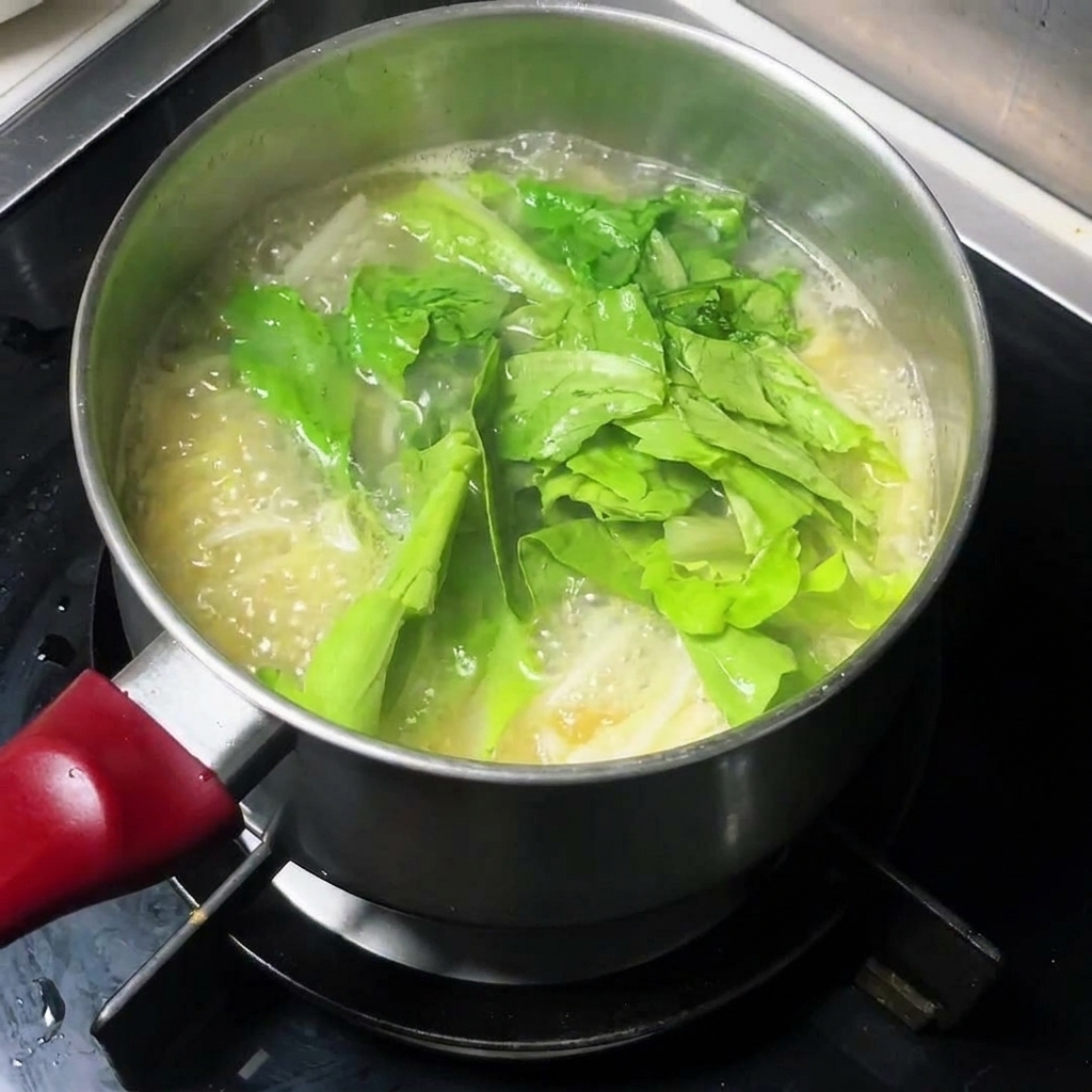 Fresh leafy greens being added to a pot of boiling noodle soup.