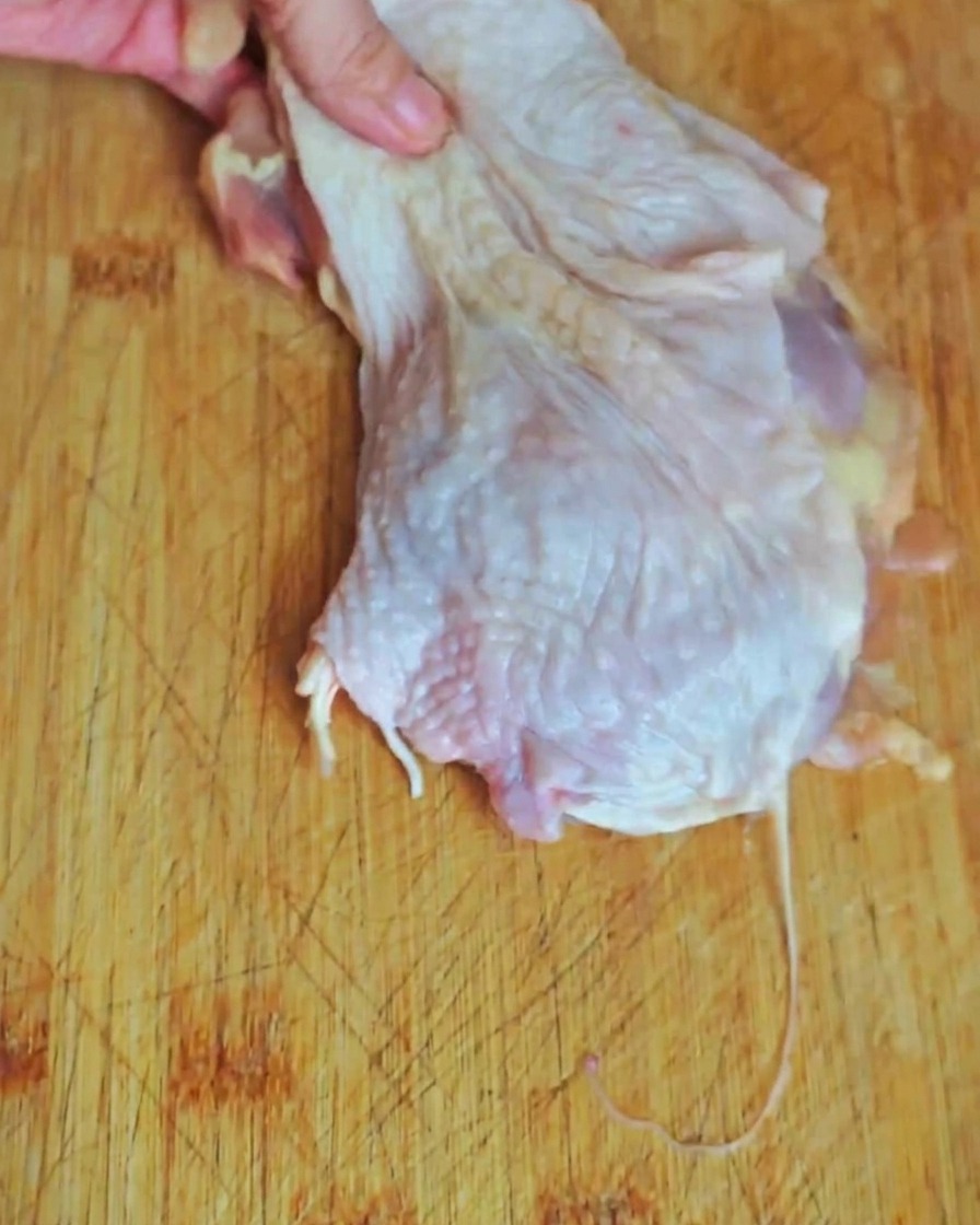 A close-up of chicken leg meat being sliced into bite-sized pieces on a wooden cutting board.