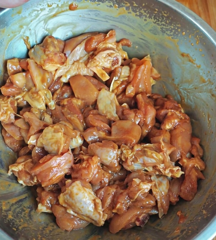 Seasoned chicken pieces marinating in a metal bowl, coated with a glossy sauce mixture.