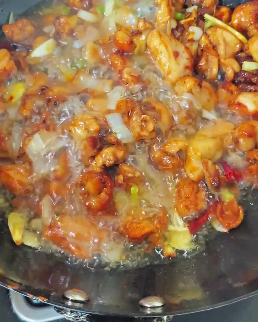 Boiling water being poured into a wok containing seared chicken and aromatics, creating a bubbling broth.