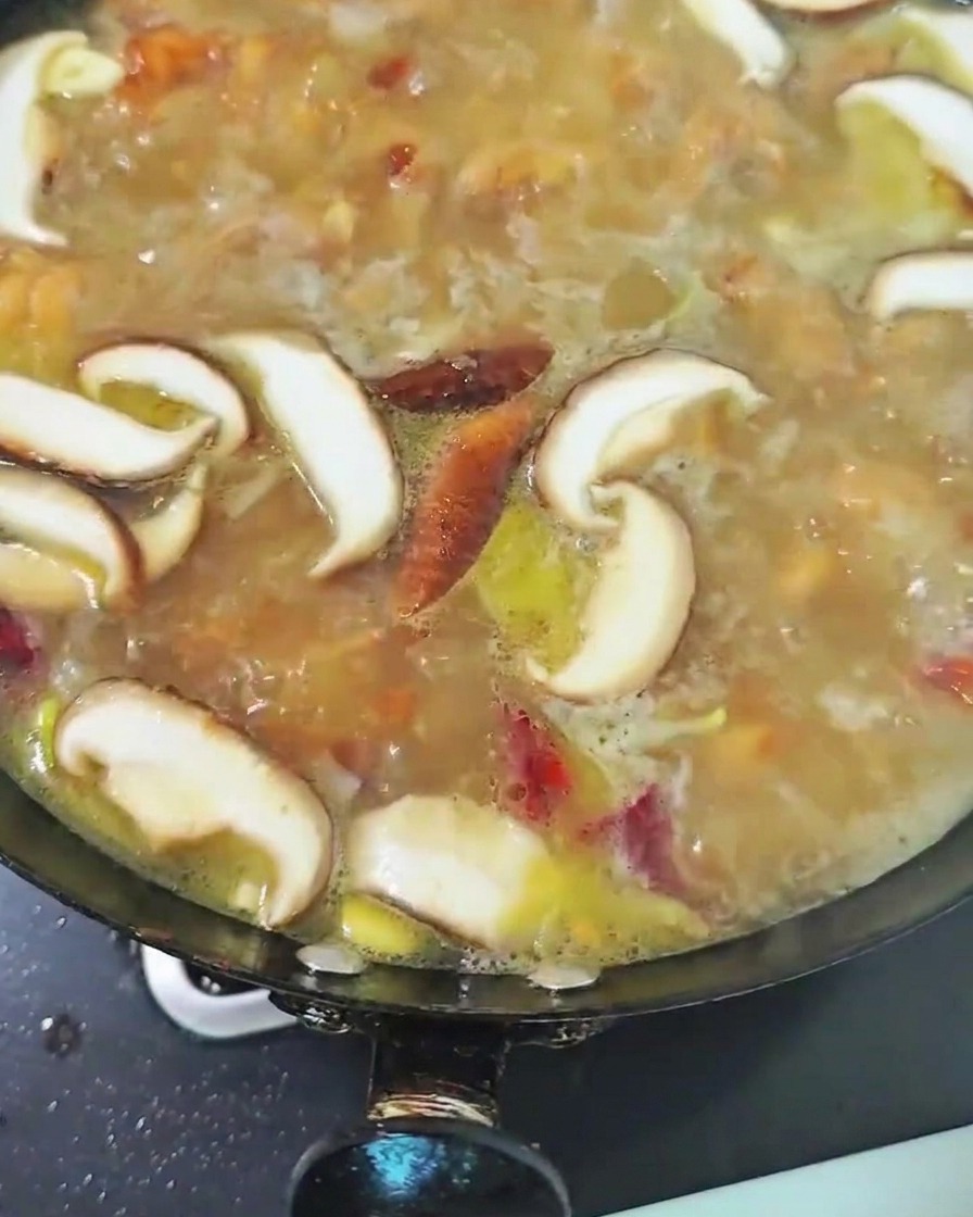 Sliced shiitake mushrooms simmering in the chicken broth inside the wok.