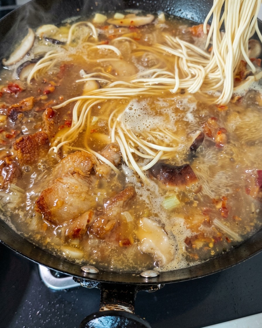 Fresh noodles being dropped into a rich, bubbling chicken and mushroom broth in a wok.