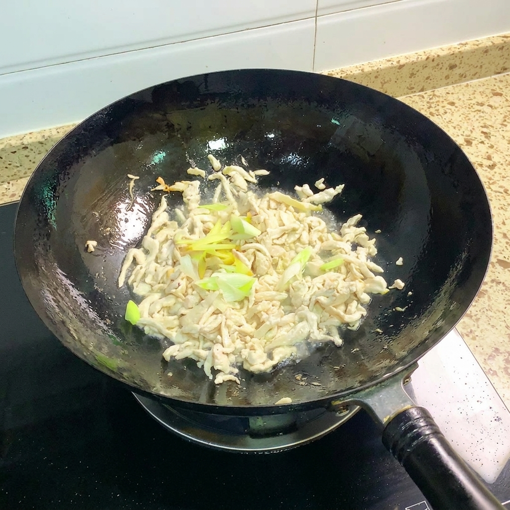 Scallions and ginger being stir-fried with cooked chicken in a wok.