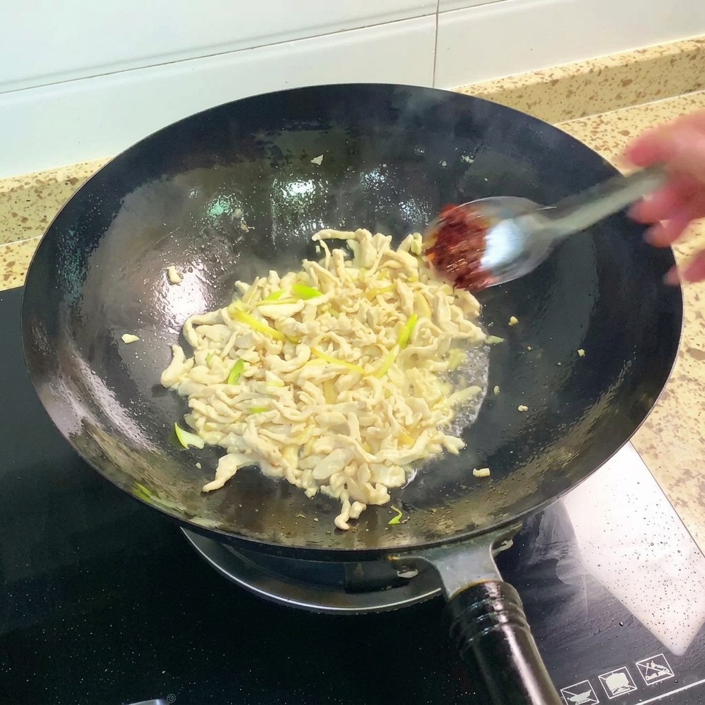 Pixian bean paste being added to the wok and stirred into the chicken mixture.