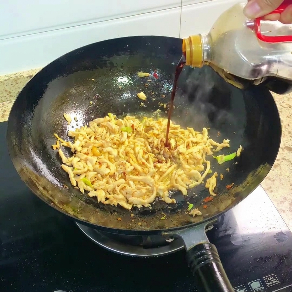Dark soy sauce being poured into the wok with the stir-fried chicken.