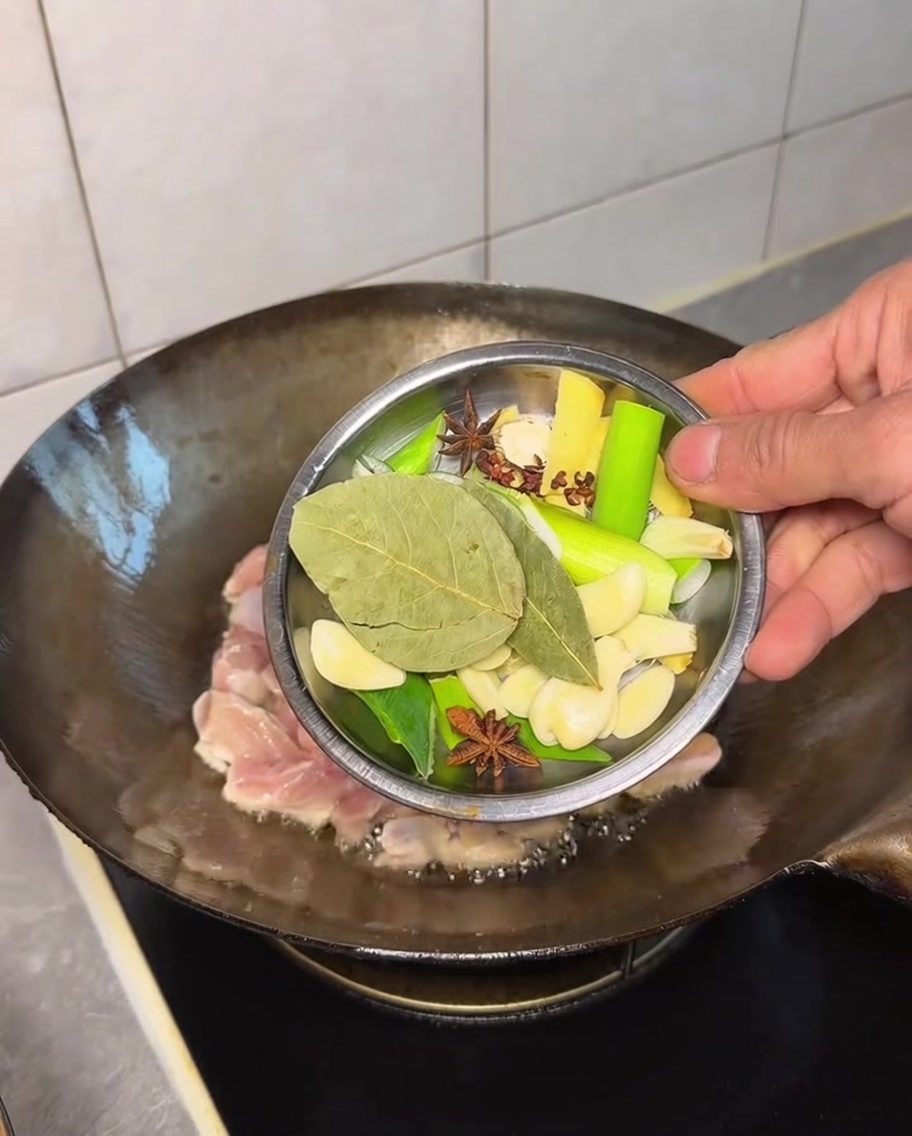 A variety of whole aromatics being added to the chicken in the wok.
