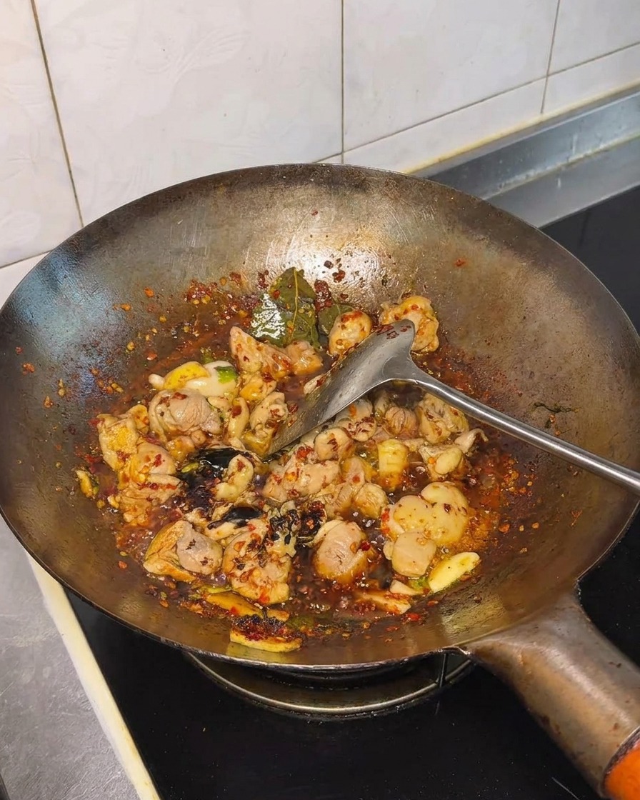 Soy sauce and seasonings being incorporated into the stir-fried chicken in the wok.