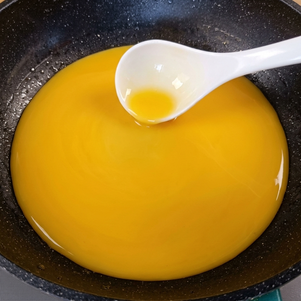A thickened golden-yellow sauce being stirred in a dark pan with a white ladle.