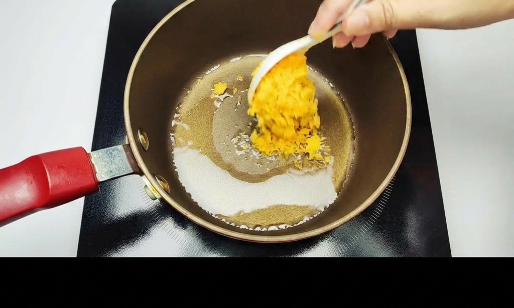 A hand using a white spoon to stir-fry mashed golden salted egg yolks in a dark non-stick pot.