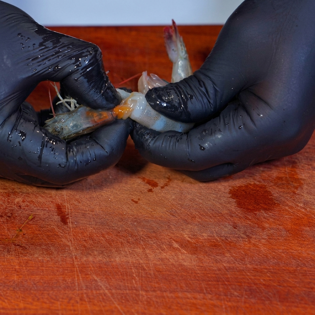Peeling the shells off raw shrimp on a wooden cutting board.
