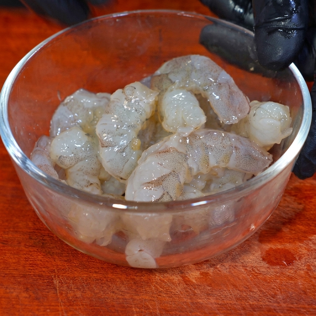 Shrimp marinating in a glass bowl with seasoning and cornstarch.