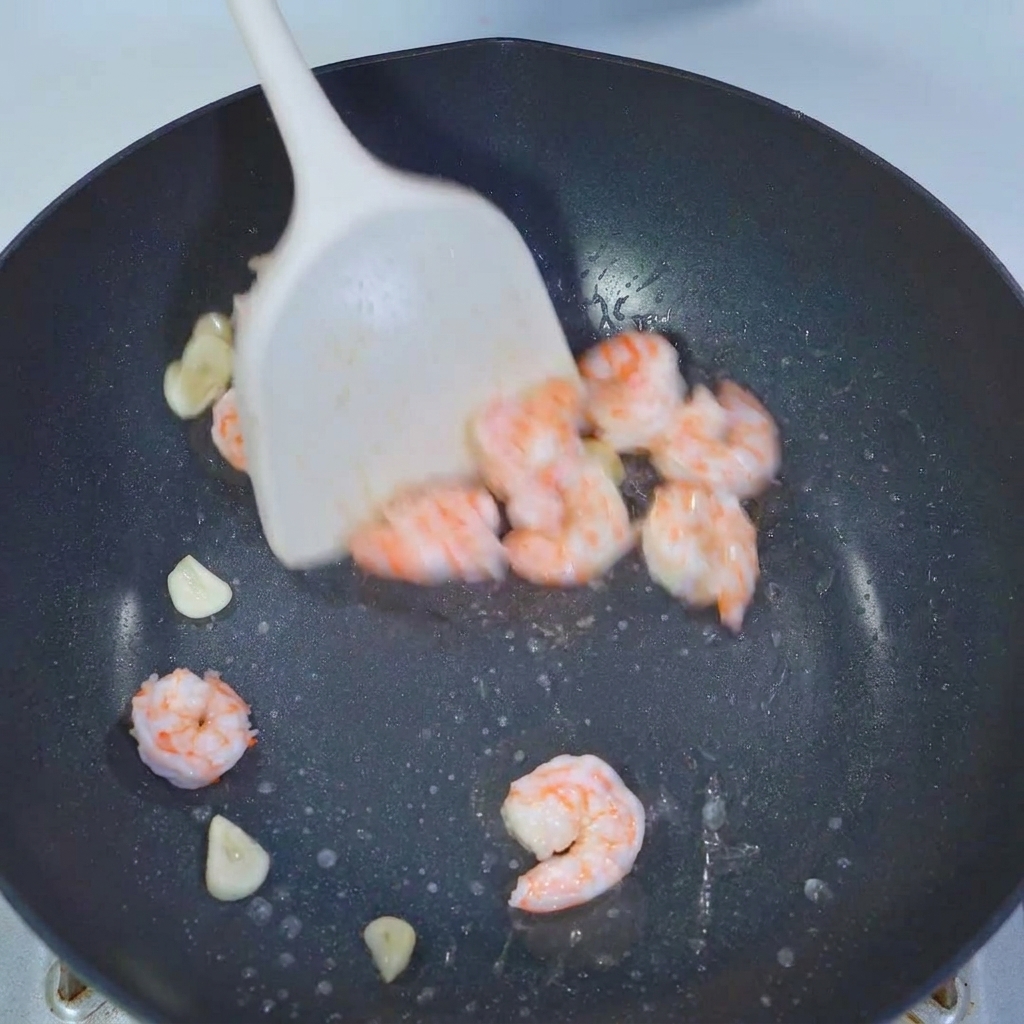 Okra pieces being tossed in a pan with shrimp and garlic using a white spatula.