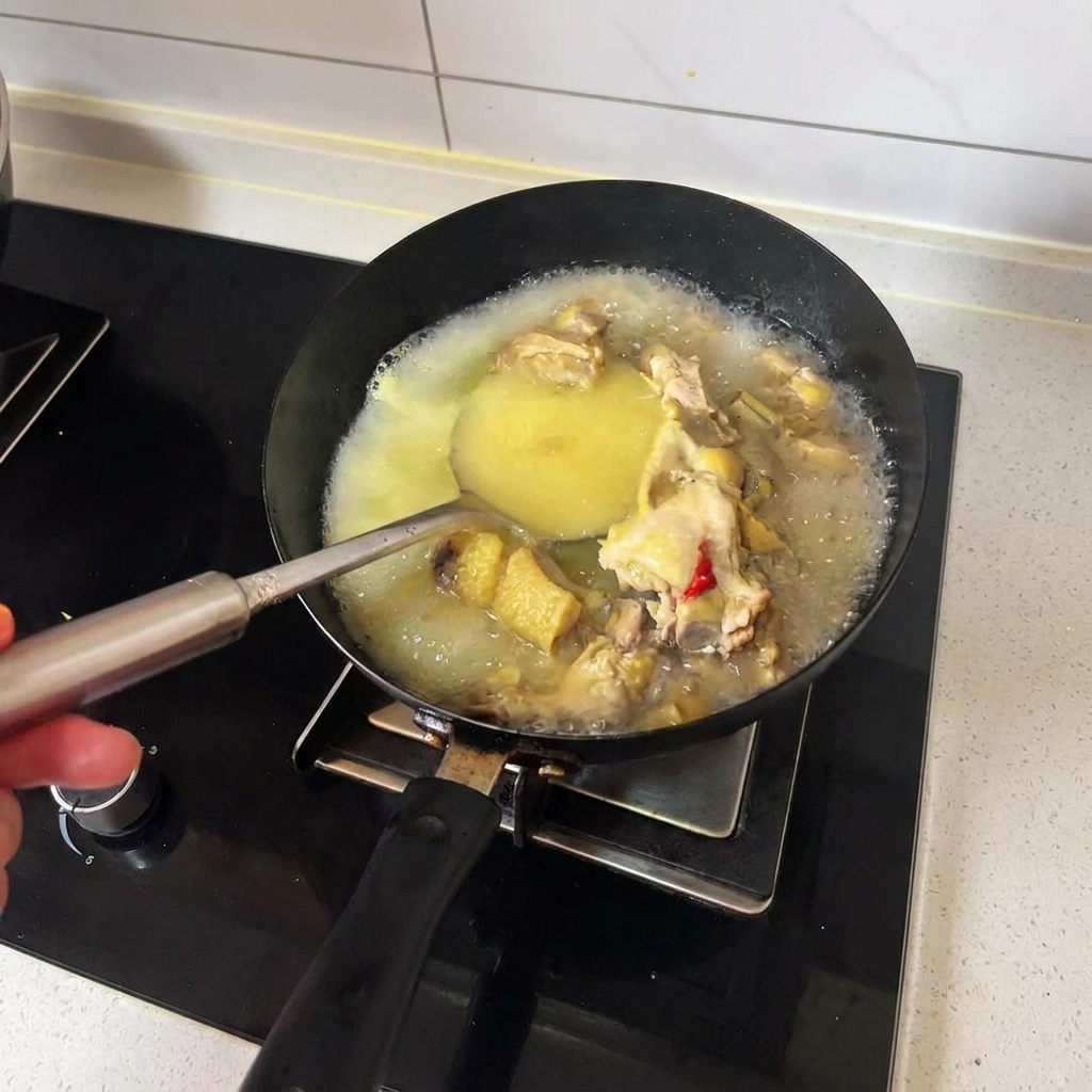 A ladle stirring hot golden chicken broth and cooked chicken pieces in a black wok.
