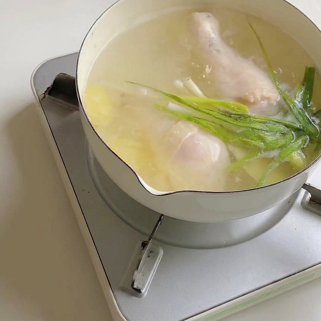 Ramen seasoning powder being stirred into the pot of broth with chicken.