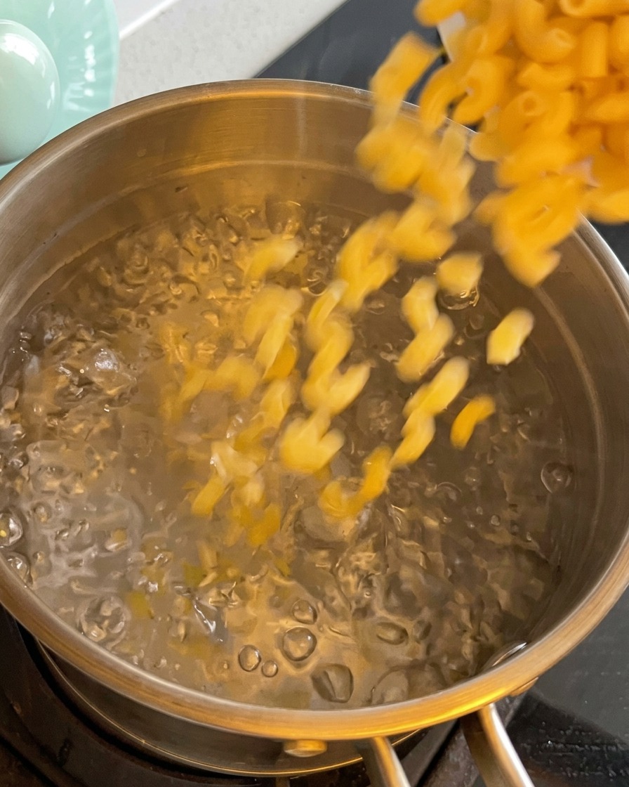 Dry macaroni pasta being poured into a pot of boiling water.