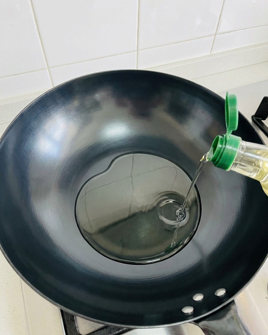 Olive oil being poured into an empty, heated dark wok.