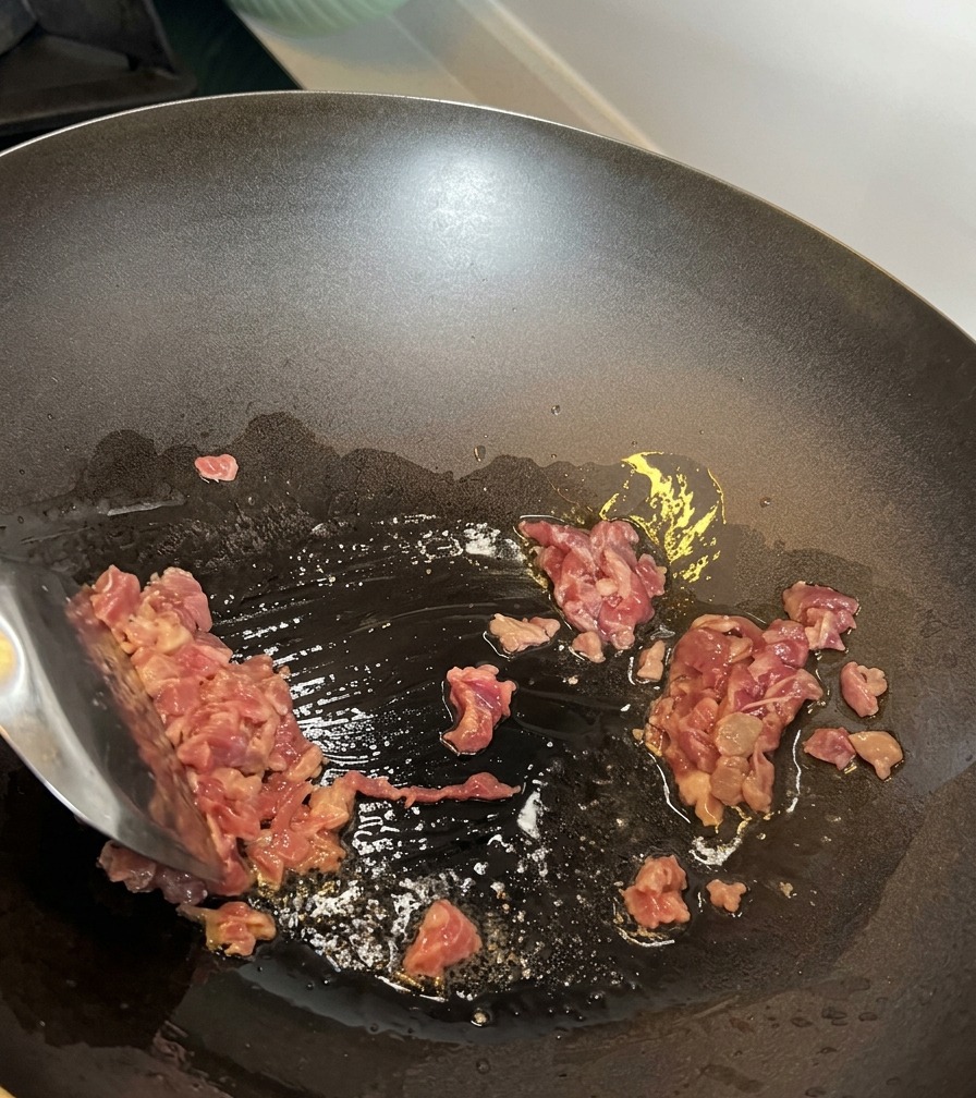 Diced beef pieces being stir-fried in a hot wok.