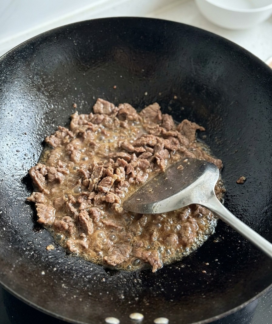 Freshly diced tomatoes being added to browned beef in a wok.