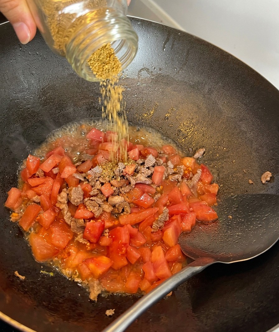 Sea salt being sprinkled over a mixture of sautéed beef and diced tomatoes.