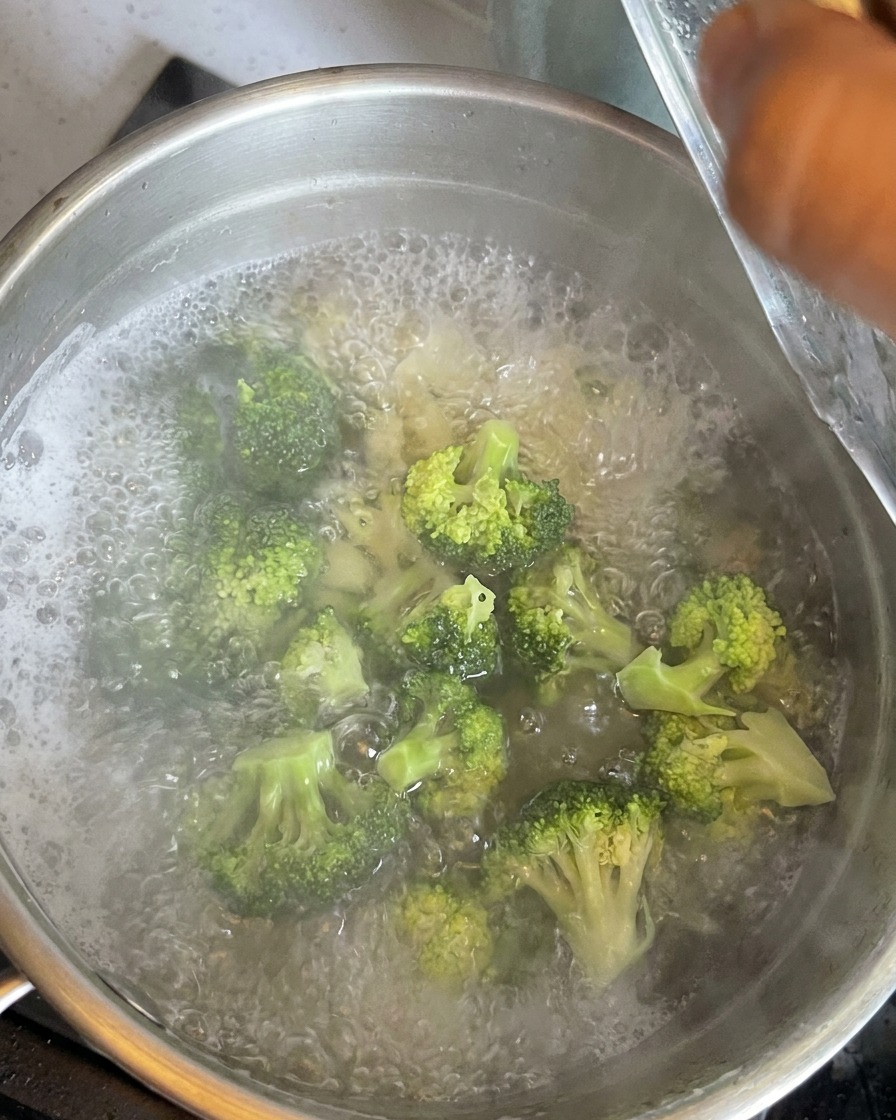 Bright green broccoli florets submerged in boiling water with cooking macaroni.